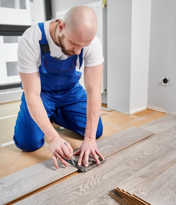 A male worker drawing a line and cutting the wood plank for the floor installation.